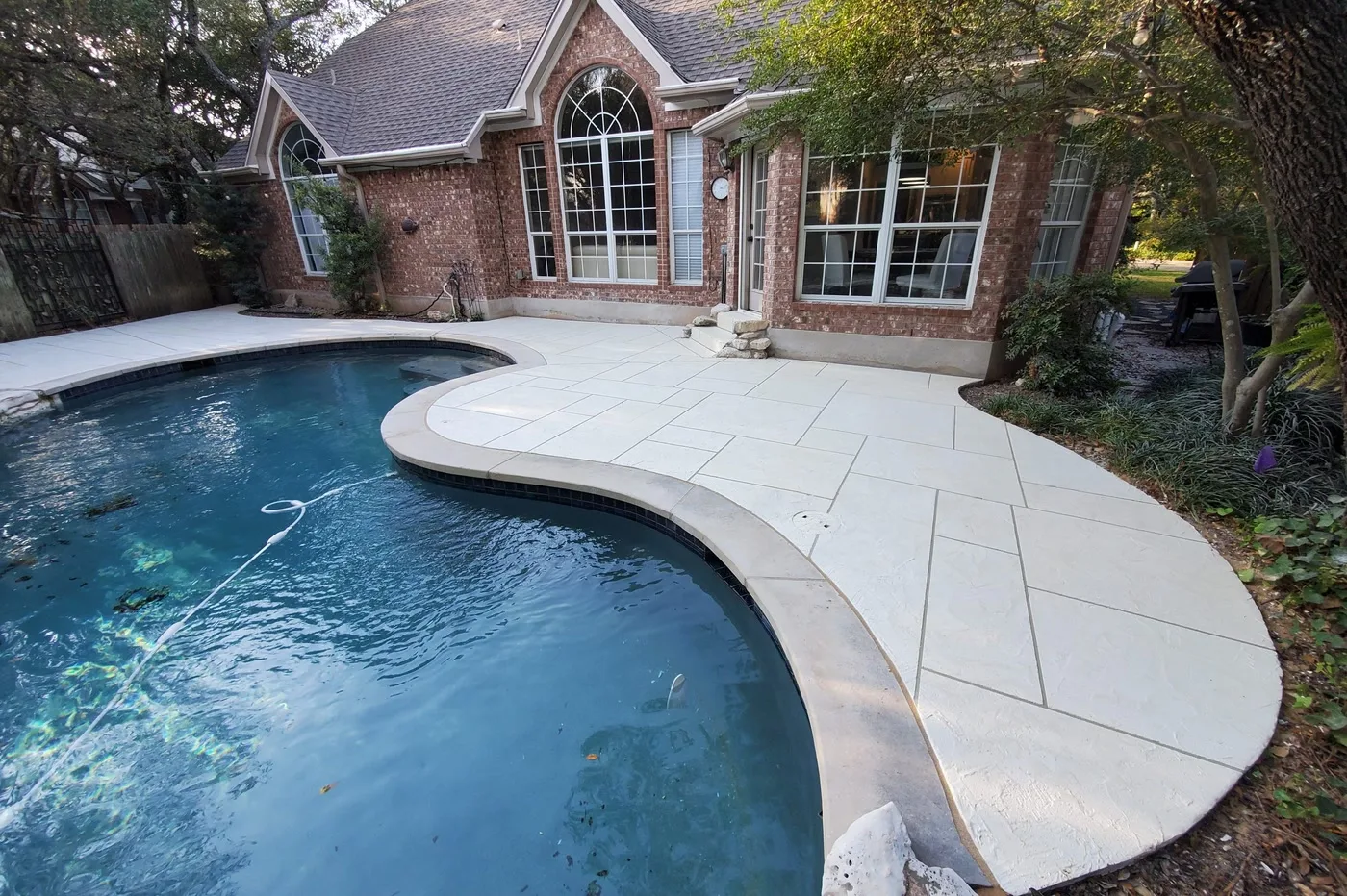 Light-colored concrete pool deck with scored panels wrapping a kidney-shaped pool