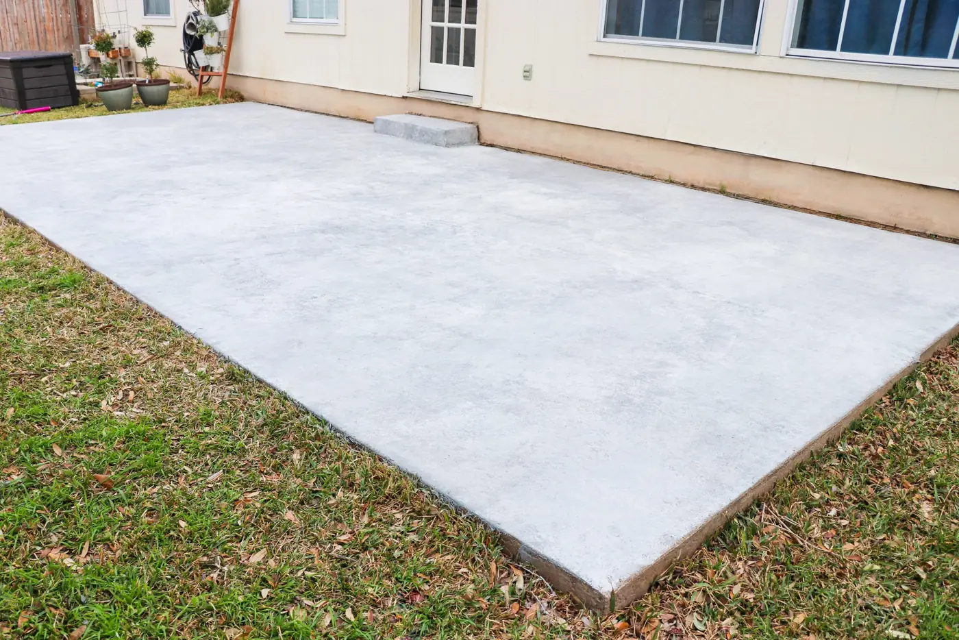 Resurfaced concrete patio with a smooth, even gray surface behind a house, edged by lawn